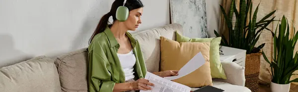 A woman in casual attire sits on a couch with headphones on, enjoying music. — Stock Photo