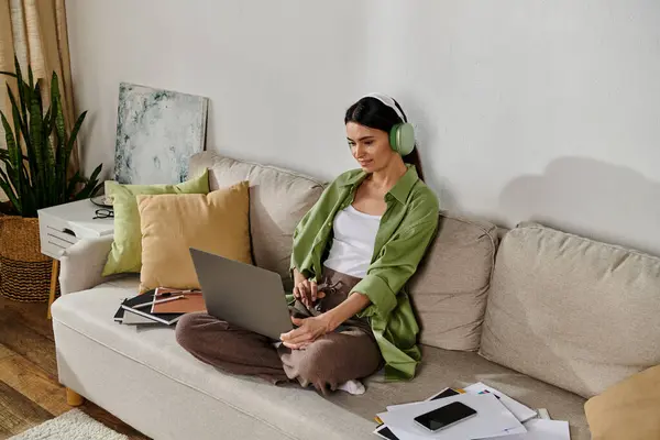 Donna in abbigliamento casual multitasking sul divano con laptop. — Foto stock