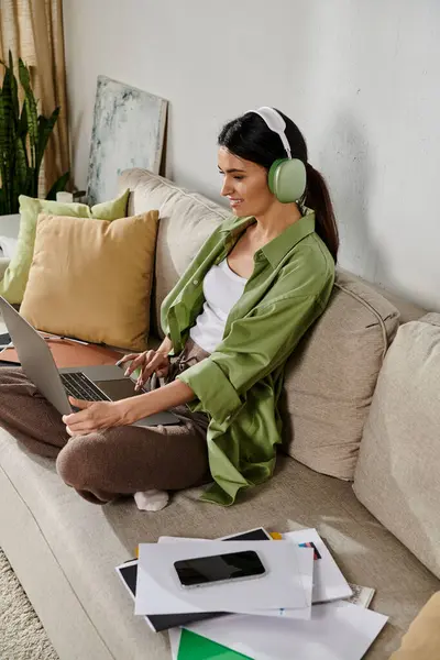 Una mujer con atuendo casual se sienta en un sofá usando una computadora portátil. - foto de stock