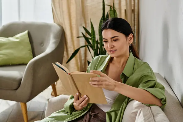 A woman in casual attire reads a book while sitting on a couch at home. — Stock Photo