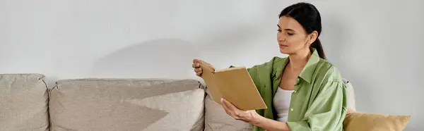 Elegant woman in casual attire sitting on couch, holding a book. — Stock Photo