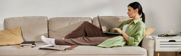Eine Frau in Freizeitkleidung arbeitet auf einem Laptop, während sie auf einer Couch sitzt. — Stockfoto