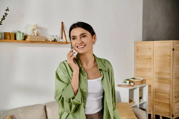A woman in casual attire standing in a living room, chatting on a cell phone. — Stock Photo
