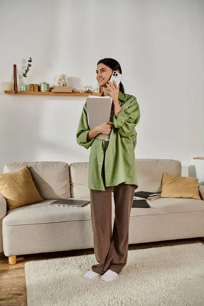 A woman in casual attire stands in a cozy living room, absorbed in a phone call. — Stock Photo
