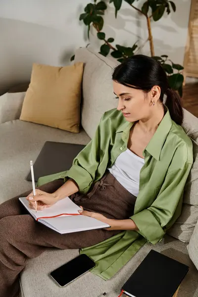 Frau sitzt und schreibt in Notizbuch auf Couch. — Stockfoto