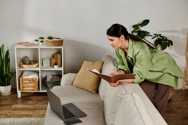 A woman in casual attire sitting on a couch engrossed in notebook. — Stock Photo