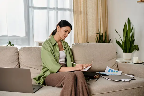 Woman in casual attire works on laptop while seated on a couch. — Stock Photo