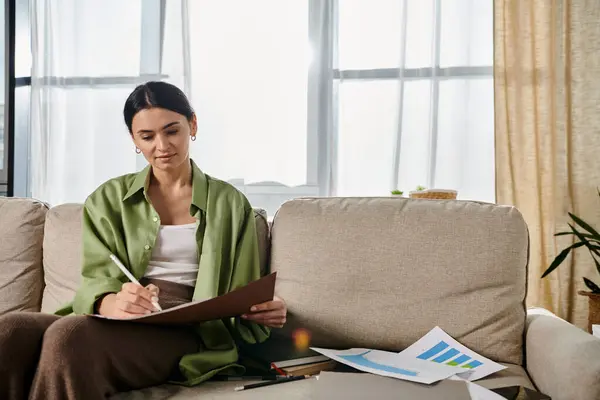 Woman in casual attire sitting on couch, holding pen and paper. — Stock Photo