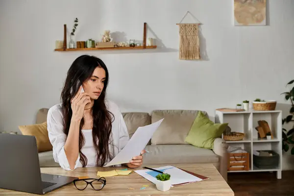 A woman in casual attire works on her laptop at a table with papers. — Stock Photo