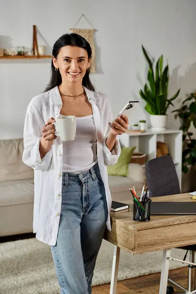 Eine Frau in Freizeitkleidung balanciert eine Tasse Kaffee, während sie ihr Handy kontrolliert. — Stockfoto