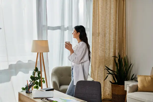 A woman in casual attire stands by a window in a living room. — Stock Photo