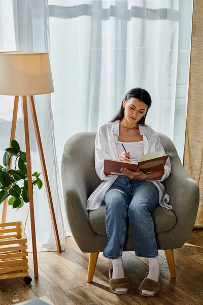 Eine Frau liest friedlich ein Buch, während sie im bequemen Stuhl sitzt. — Stockfoto