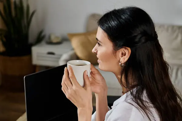 A woman in casual attire sits at a table, savoring a cup of coffee. — Stock Photo