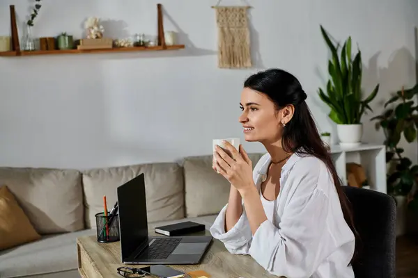 A stylish woman in casual attire is focused on her laptop at a table. — Stock Photo