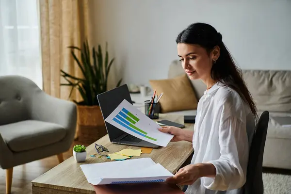 Una donna in abbigliamento casual si siede a un tavolo, assorta nel lavoro sul suo computer portatile. — Foto stock