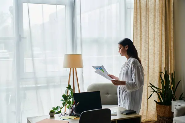 Une femme se tient devant un ordinateur portable, travaillant à la maison. — Photo de stock