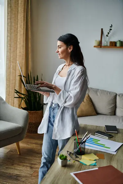 Una mujer con estilo en una sala de estar, sosteniendo un ordenador portátil. - foto de stock