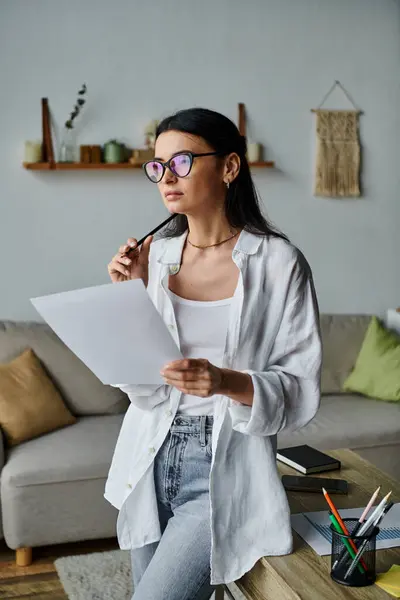 A woman in casual attire sits on a couch, holding a pen and paper. — Stock Photo