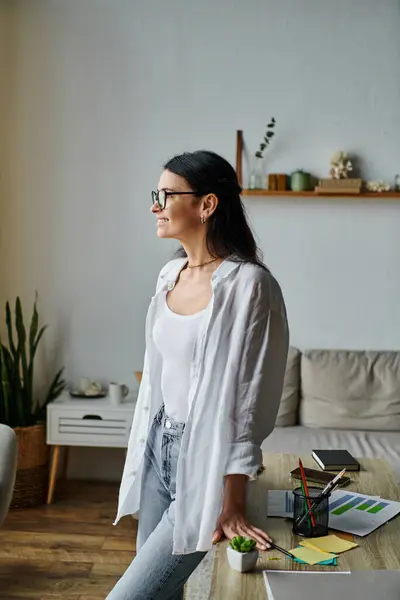 Uma mulher na moda em trajes casuais fica ao lado de um sofá em uma sala de estar moderna. — Fotografia de Stock