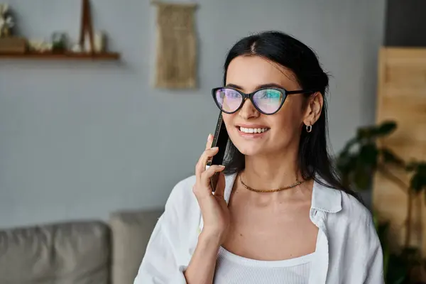 Una donna con gli occhiali parla al cellulare mentre lavora da casa. — Foto stock