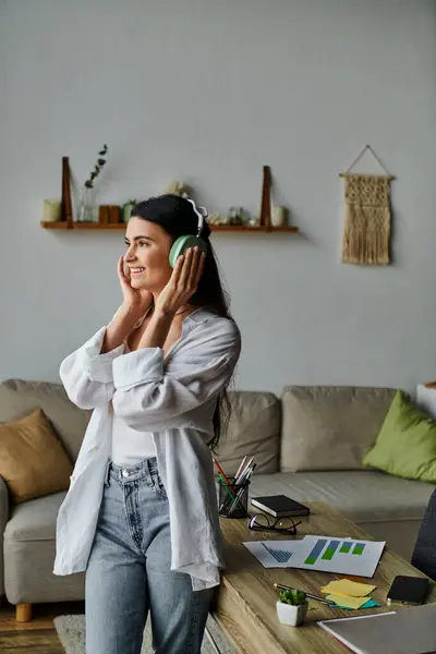 A woman stands in a living room, immersed in music through headphones. — Stock Photo