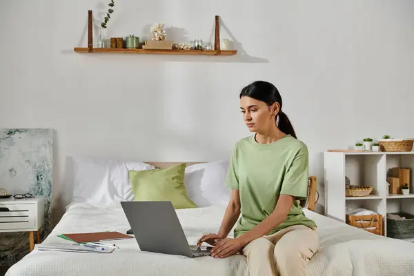 Woman in casual attire working on laptop while sitting on bed. — Stock Photo
