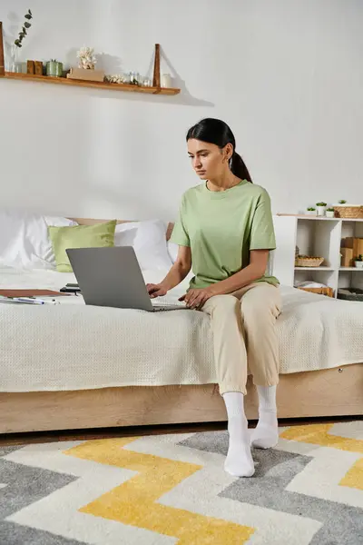 Mujer con atuendo casual sentada en la cama, centrándose en la pantalla del ordenador portátil. - foto de stock