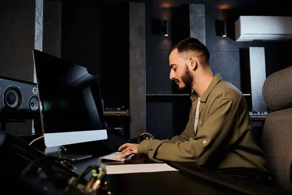 Un uomo si siede ad una scrivania in uno studio di registrazione, concentrato sul mixare musica per le prove di una band. — Foto stock