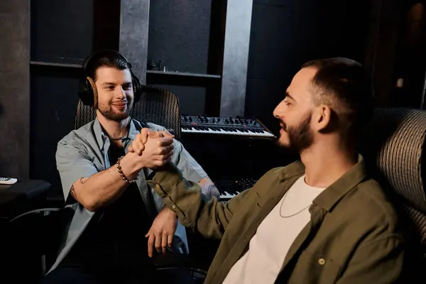Two men in a recording studio, one wearing headphones, shaking hands in agreement during a music band rehearsal. — Stock Photo