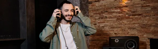 Bearded man passionately holds headphones during music band rehearsal in recording studio. — Stock Photo