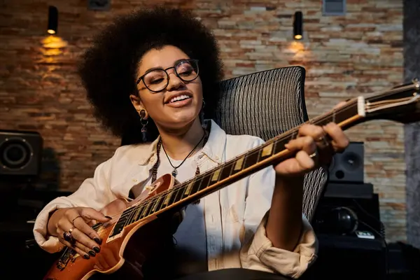 Una donna con gli occhiali strumenta una chitarra in uno studio di registrazione durante le prove di una band musicale. — Foto stock