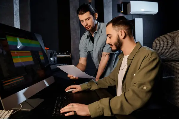 Dos hombres están colaborando en una computadora en un estudio de grabación, trabajando en la música para su ensayo de la banda. - foto de stock