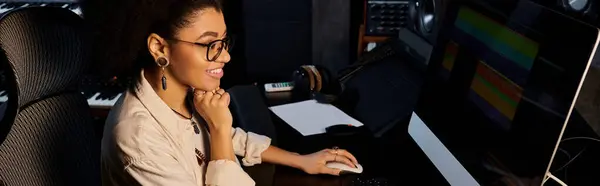 Una mujer inmersa en su trabajo, sentada en una computadora en un estudio de grabación durante un ensayo de la banda de música. - foto de stock