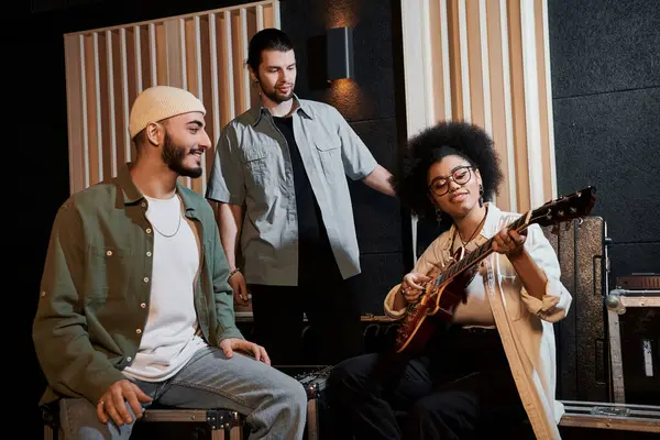 Three individuals sitting in a recording studio, immersed in playing a guitar and creating music together. — Stock Photo