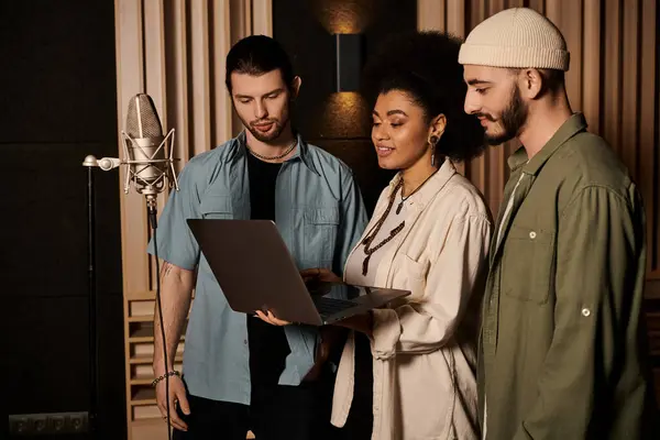 Tres individuos colaborando en un estudio de grabación, revisando música en la pantalla de un portátil. - foto de stock