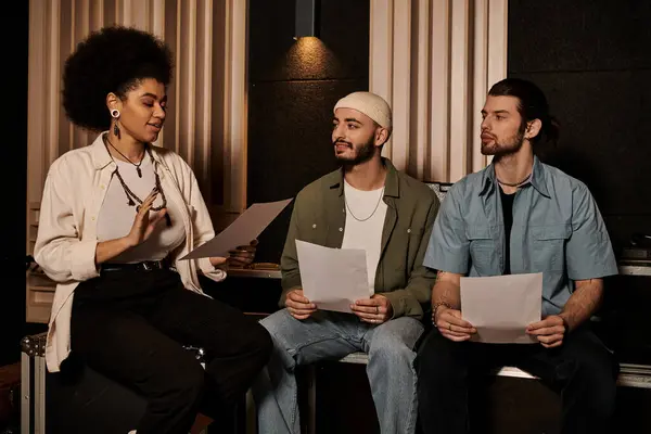 Три музыканта сидят в студии звукозаписи, держат в руках ноты и обсуждают свою следующую песню. — стоковое фото