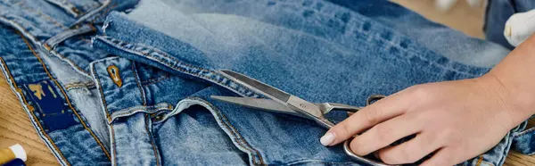 A person upcycles jeans by cutting them with scissors. — Stock Photo