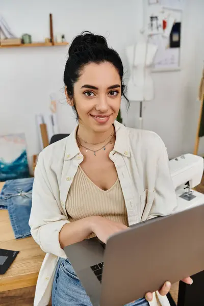 Woman in chair, holding laptop, engaged in upcycling clothes. Eco-friendly lifestyle. — Stock Photo