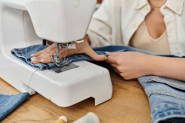 Una mujer joven con atuendo casual creando vaqueros upcycled en una máquina de coser. - foto de stock
