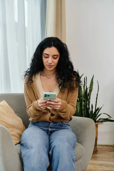 A woman in casual attire sitting on a couch, absorbed in her cell phone. — Stock Photo