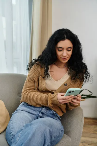 Woman in casual attire sitting on couch, absorbed in cell phone screen. — Stock Photo