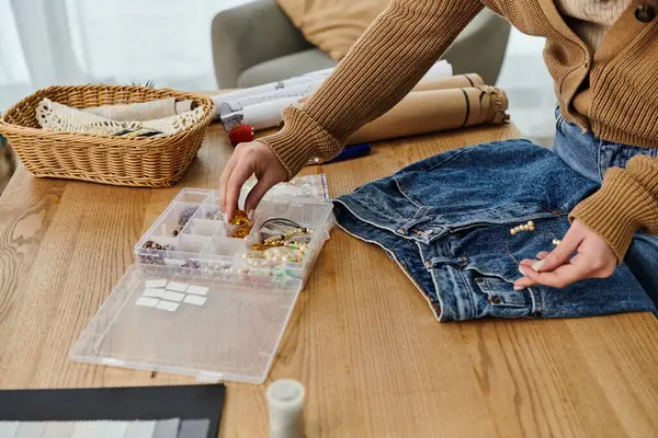 Woman in casual attire upcycling clothes, arranging beads in a basket. — Stock Photo