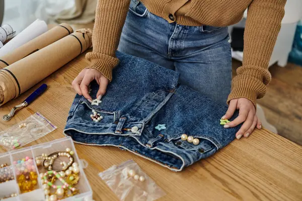 Woman in brown sweater adding beads to jeans. — Stock Photo