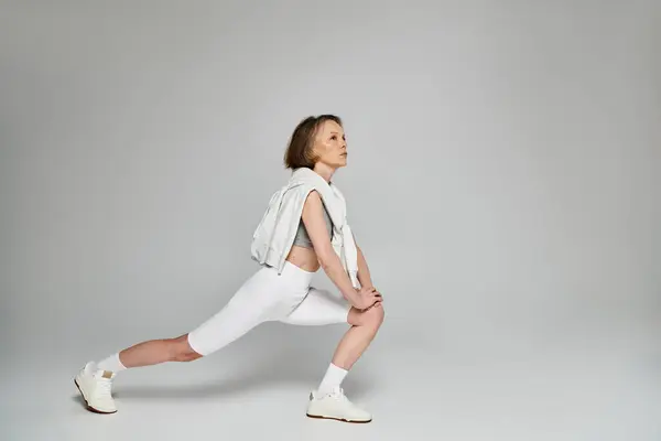 Mature woman in comfortable attire performing a squat on a white background. — Stock Photo