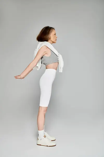 Una mujer madura en traje cómodo se para con los brazos extendidos, posando activamente. - foto de stock