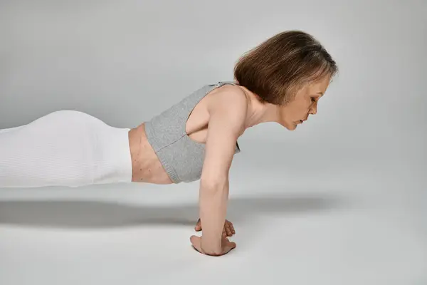 Attractive woman in comfy attire energetically doing push ups on white background. — Stock Photo
