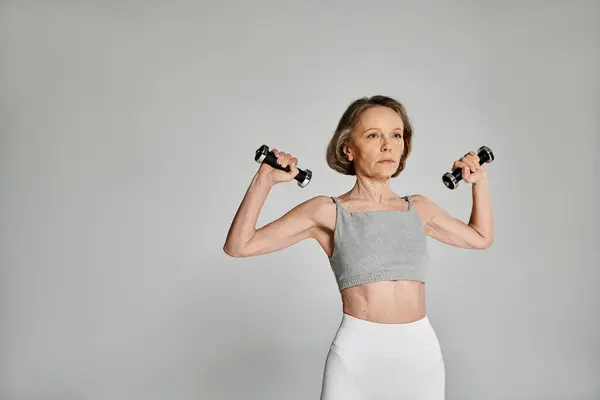 Attractive woman in active pose with dumbbells on gray background. — Stock Photo
