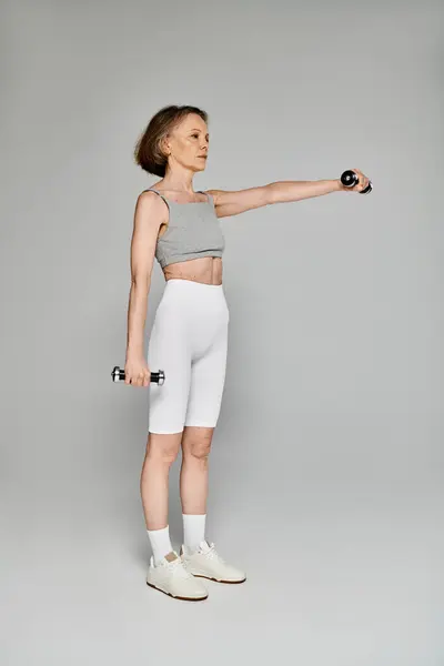 A mature, attractive woman in comfortable attire confidently holds a pair of dumbbells. — Stock Photo