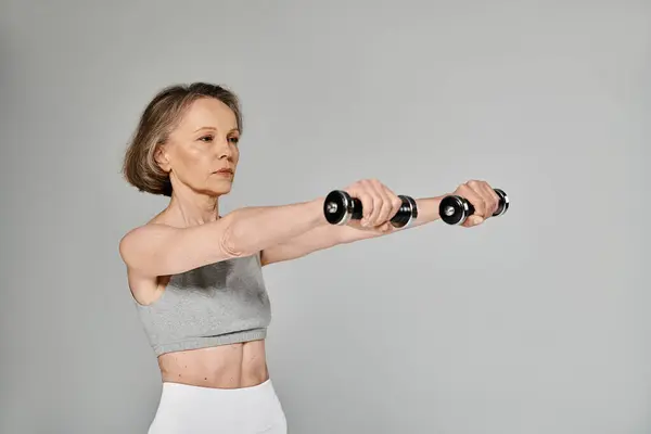 Elderly lady doing dumbbell exercises on gray background. — Stock Photo