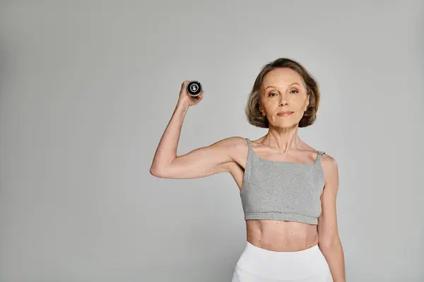 A mature, attractive woman in comfy attire showcases graceful strength while posing with a dumbbell. — Stock Photo